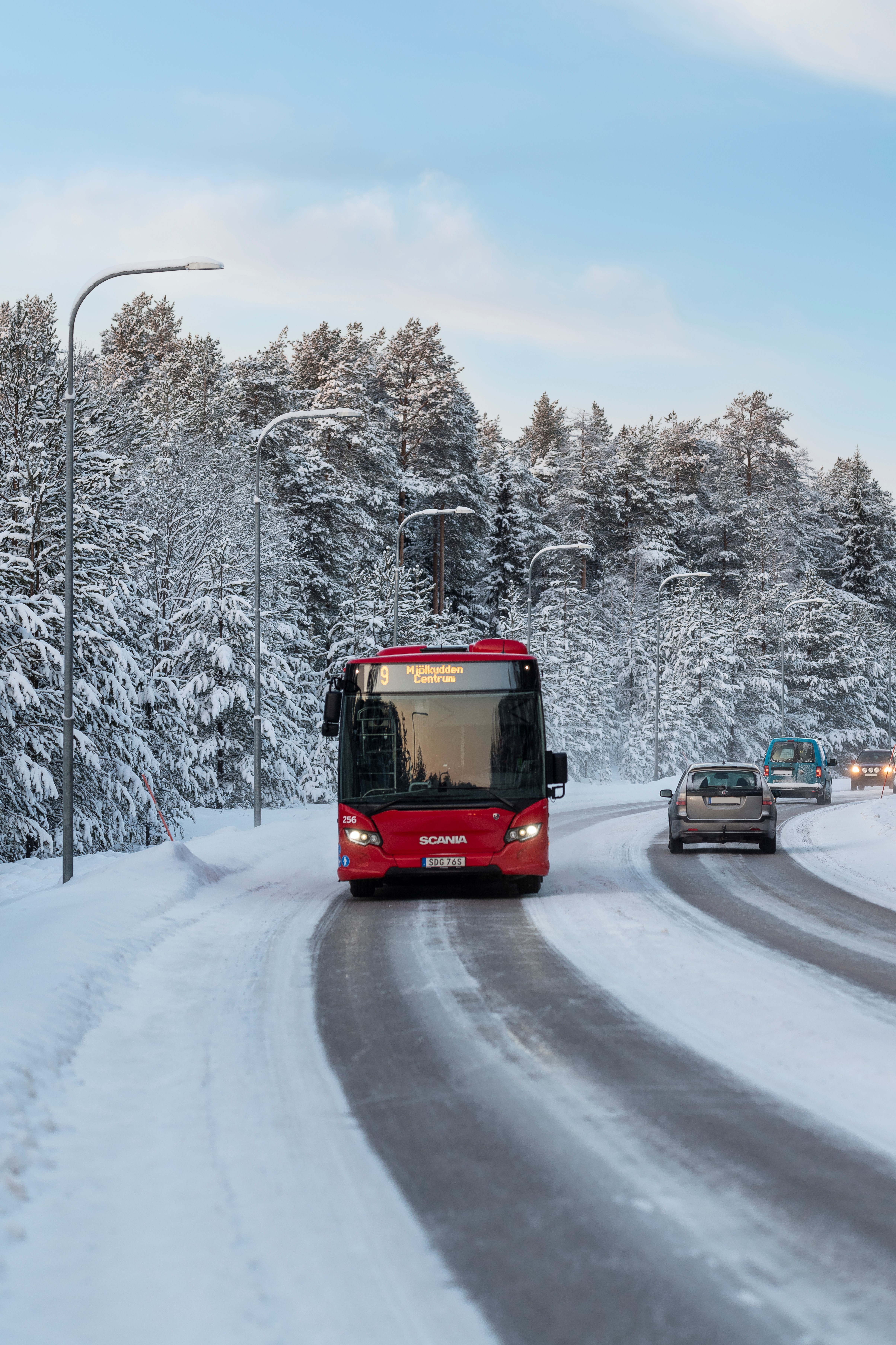 Linje 9 trafikerar snötäckta gator med träd i vinterskrud bakom.